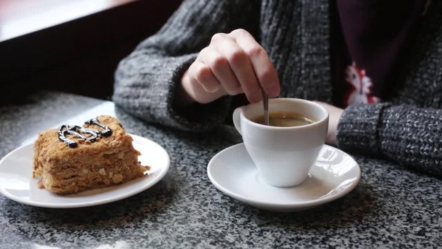 The girl stirs sugar in a white cup of coffee. Female hands with a cup of americano of espresso.