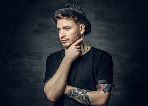 Thoughtful male with crossed tattooed arms, dressed in a black t shirt and tweed hat.
