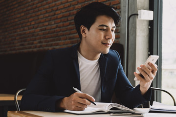 Businessman using smart phone and writing in organizer.