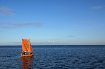 Small wooden boat with orange sail