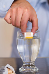 Hand drooping a pill effervescent tablet in a glass of water