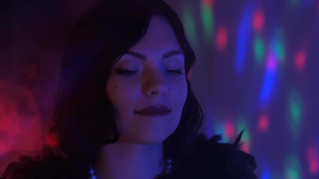 Sexy woman dressed in the style of a Great Gatsby flirting and dancing on party. Neon blue and red light.