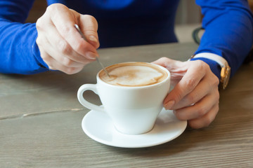 hands of the girl stirring coffee behind a little table