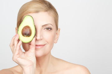 Vitamin care. Horizontal shot of a beautiful mature woman holding half of an avocado to her face smiling