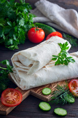 Shawarma chicken roll in a pita with fresh vegetables and cream sauce on wooden background. Selective focus