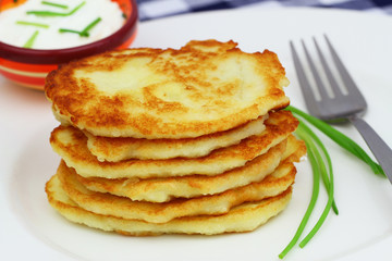 Potato fritters stacked on white plate and sour sauce in bowl
