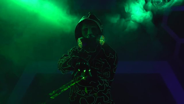 Humanoid man robot with laser weapon in clouds of smoke in darkness.