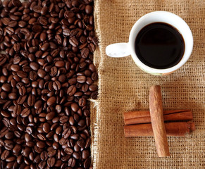 Coffee cup on jute bag with cinnamon sticks and coffee beans