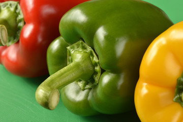 Red, green and yellow bell peppers on green chopping board