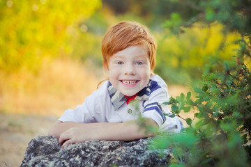 Cute red hair boy smiling to camera and standing in forest