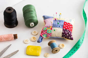 Fototapeta na wymiar closeup sewing tools , patchwork, tailoring and fashion concept - thread spools, buttons, measuring tape, pincushion, scissors, pieces of colored patchwork fabric, soap on white desk