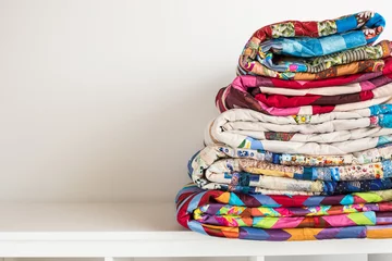 näh- und modekonzept - stapel bunter quilts, schöne bettdecken, die in mehreren reihen in der höhe zur lagerung gestapelt sind, verkaufs-patchwork-produktionen auf weißem hintergrund, kopierraum © melnikofd