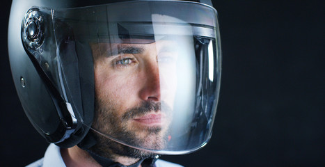 Fototapeta premium Portrait of a professional rider or motorcyclist, in a protective black helmet, on a black background. Concept: driver, drive, speed, protection, protective suit, reaction, love of extreme sports. 