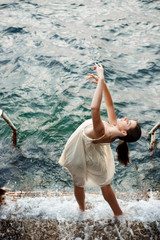 Young beautiful ballerina dancing and posing outside, sea background.