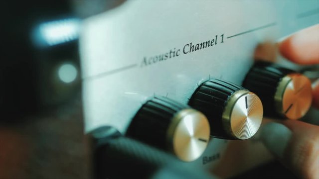 Men's hands twist tumblers on control panel of guitar amplifier. A mode switch being switches on amp. Man's hand inserts cable jack in guitar amp