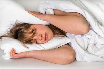 Fototapeta na wymiar Woman trying to sleep, she covering ears with pillow