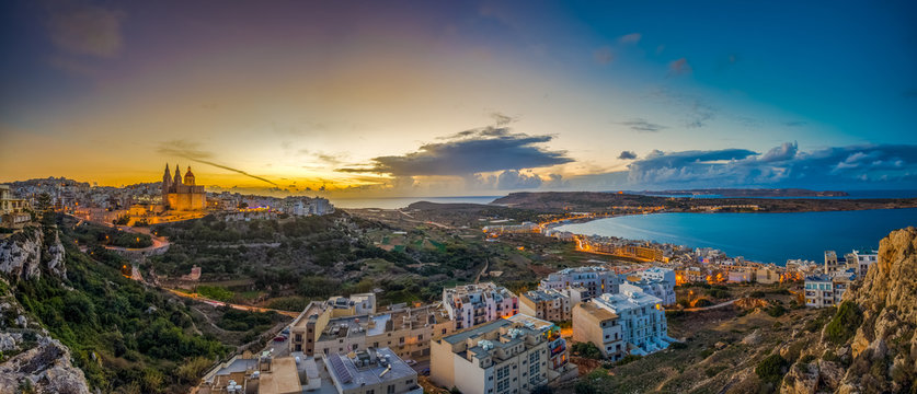 Il-Mellieha, Malta - Beautiful panoramic skyline view of Mellieha town at sunset with Paris Church and Mellieha beach at background with blue sky and clouds