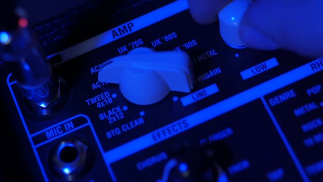 Men's hands twist tumblers on control panel of guitar amplifier. A mode switch being switches on amp. Man's hand inserts cable jack in guitar amp. Neon light, Concert.