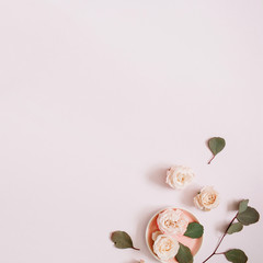 Beige roses and eucalyptus branches on pale pastel pink background. Flat lay, top view. Floral texture background.