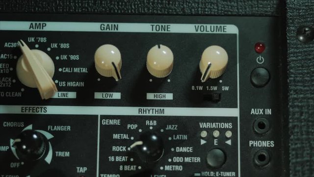Men's hands twist tumblers on control panel of guitar amplifier. A mode switch being switches on amp. Man's hand inserts cable jack in guitar amp