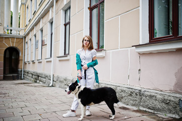 Naklejka na ściany i meble Trendy girl at glasses and ripped jeans with russo-european laika (husky) dog on a leash, against street of city. Friend human with animal theme.