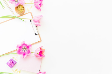 Beauty blog concept. Freelancer or blogger workspace with clipboard, notebook, pink tulips and accessories on white background. Flat lay, top view.