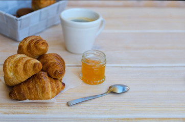 Cup of coffee, small milk jug  and croissants with peach jam on rustic wood table. Traditional French breakfast. Copy space.