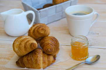 Cup of coffee, small milk jug  and croissants with peach jam on rustic wood table. Traditional French breakfast.