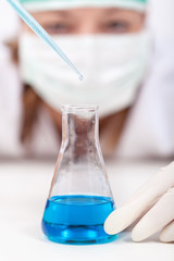 Laboratory technician dropping reagent into an erlenmeyer flask