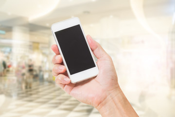 Hand holding mobile phone with abstract blur shopping mall background