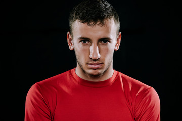 Close up portrait of handsome Caucasian sportsman wearing red sportswear and posing after exercises on dark background. Healthy inspirational fitness lifestyle, sport motivation. 