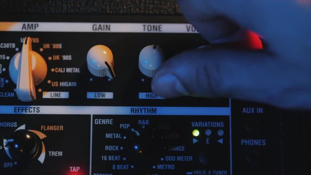 Men's hands twist tumblers on control panel of guitar amplifier. A mode switch being switches on amp. Man's hand inserts cable jack in guitar amp