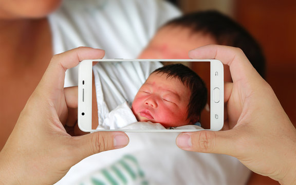 Hands taking picture of Newborn baby with smartphone.