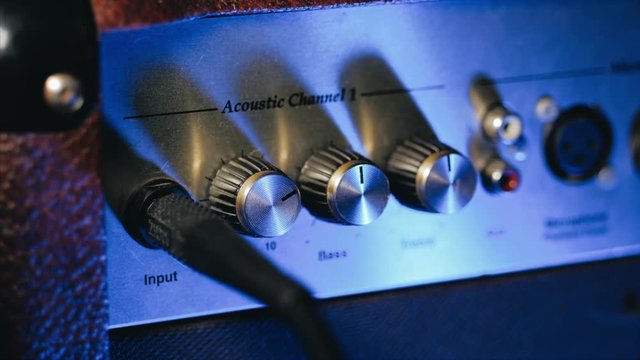 Men's hands twist tumblers on control panel of guitar amplifier. A mode switch being switches on amp. Man's hand inserts cable jack in guitar amp
