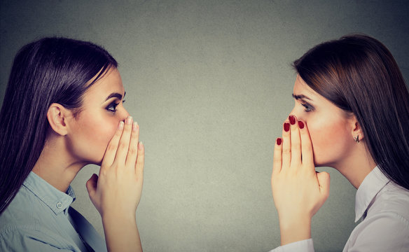 Two women whispering a gossip secret to each other