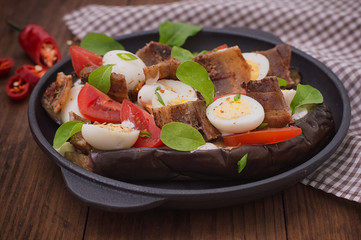 Baked eggplant with bacon, garlic and quail eggs on pan. Wooden background. Top view. Close-up