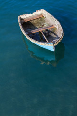 Looking down from above onto a small, blue rowing boat that has broken away from it's moorings and is floating away on a calm ocean.