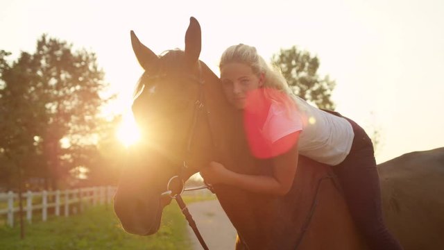 SLOW MOTION CLOSE UP DOF Beautiful blonde girl laying her head against horse's neck and embracing her beloved mare. Pretty young woman bareback riding stunning gelding on tranquil sunny summer morning
