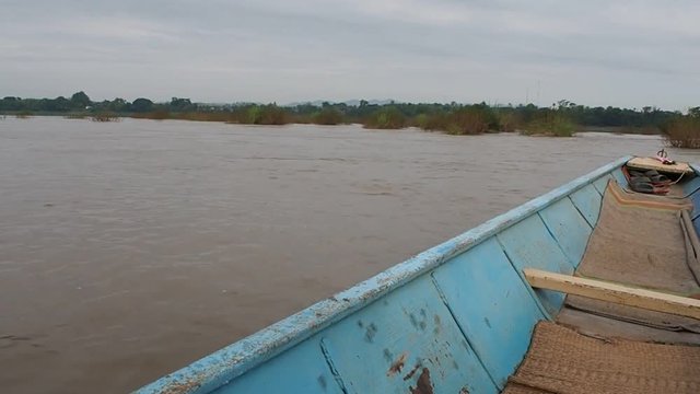 Wide angle view of a blue wooden boat stearing around aquatic plants to an island on the Mekong River. Loei, Thailand. Travel and nature concept.