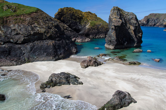 A landscape image of the tourist attraction Kynance Cove in Cornwall UK which has rugged, cliffs and dark caves and white sandy beaches and maintained by The National Trust.
