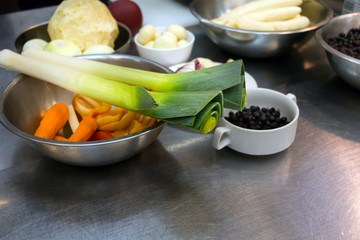 Green leek, fresh peeled vegetables, roots ready for cooking on metal kitchen table. Vegetarian diet. Helathy eating concept. Copy space.