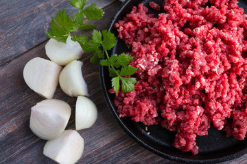 Raw red minced meat on cast iron pan with parsley and peeled cut onions. Top view.