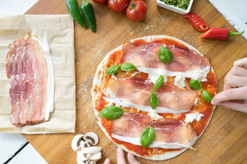 Traditional Italian pizza dough flat bread making tomato sauce mozzarella cheese salami prosciutto ham sausage basil hands chef wooden board kitchen preparation