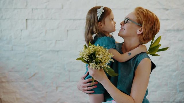 Mother and little daughter hug each other with flowers and a gift in their hands