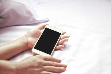 Asian woman hand holding smart phone on bed after using late at night, woman sleeping in bed with mobile phone in hand  