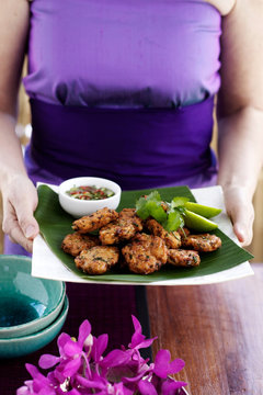 Woman carrying fishcake appetisers with coriander, lime and hot sour dipping sauce