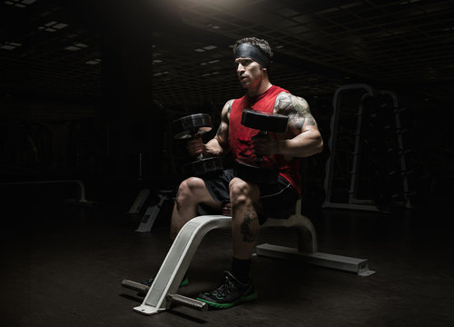 Muscular young man holding dumbbells in gym