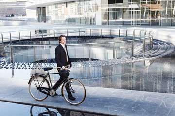 Mid adult businessman walking with bicycle by water feature in city