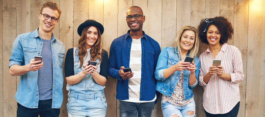Cheerful multiethnic friends looking at camera standing with phones