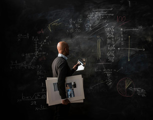 Businessman by blackboard with digital tablet and moodboard